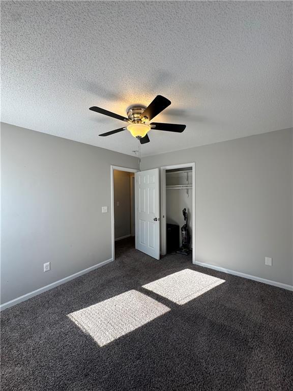 unfurnished bedroom with a textured ceiling, a closet, ceiling fan, and dark colored carpet