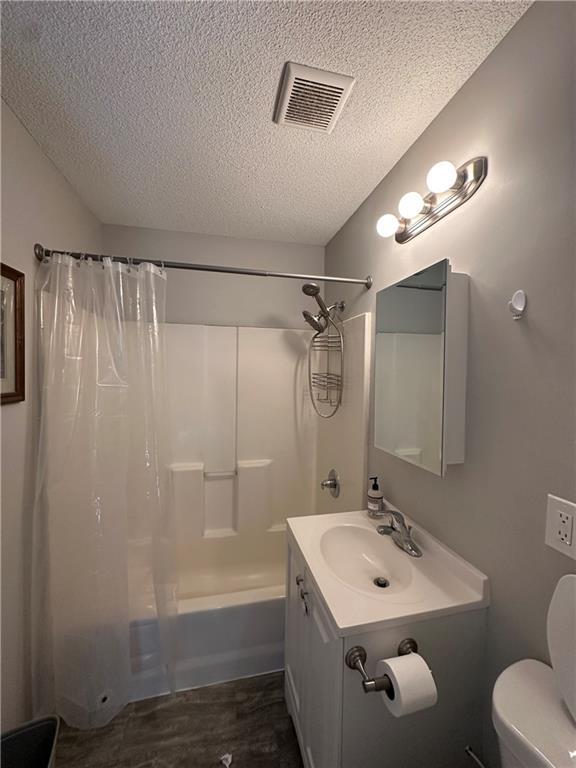 full bathroom featuring shower / tub combo with curtain, wood-type flooring, vanity, toilet, and a textured ceiling