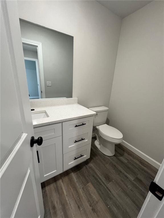 half bath with baseboards, vanity, toilet, and wood finished floors