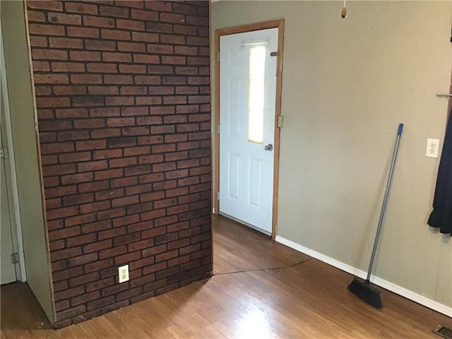 foyer entrance featuring brick wall and wood-type flooring