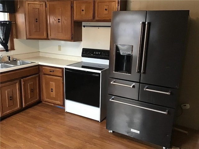 kitchen featuring high end fridge, sink, light wood-type flooring, range with electric stovetop, and range hood