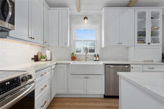 kitchen with appliances with stainless steel finishes, beamed ceiling, sink, and white cabinets