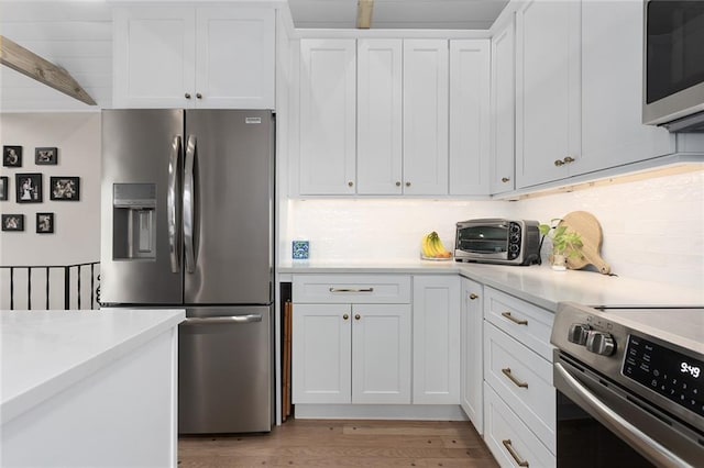 kitchen with white cabinets, light wood-type flooring, stainless steel appliances, and backsplash