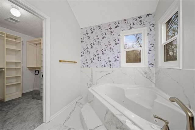 bathroom with a relaxing tiled tub and a textured ceiling