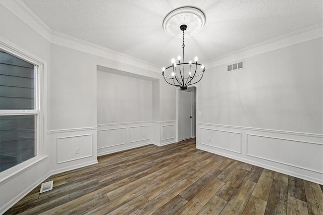 unfurnished dining area with ornamental molding, dark wood-type flooring, a notable chandelier, and a textured ceiling