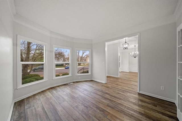 spare room featuring an inviting chandelier, ornamental molding, and dark hardwood / wood-style flooring