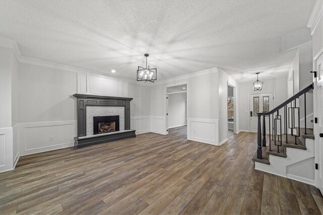 living room featuring a stone fireplace, dark hardwood / wood-style floors, an inviting chandelier, ornamental molding, and a textured ceiling