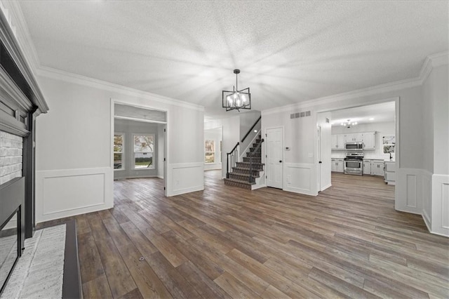 unfurnished living room with crown molding, wood-type flooring, a chandelier, a brick fireplace, and a textured ceiling