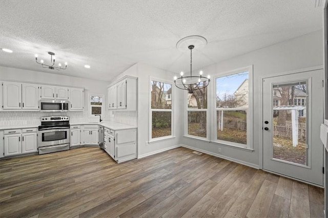 kitchen featuring pendant lighting, white cabinetry, backsplash, stainless steel appliances, and a notable chandelier