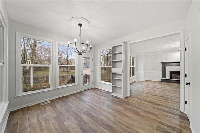 unfurnished dining area with hardwood / wood-style flooring, a textured ceiling, a notable chandelier, and a fireplace