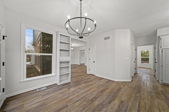 unfurnished dining area with dark hardwood / wood-style floors, a textured ceiling, and a chandelier