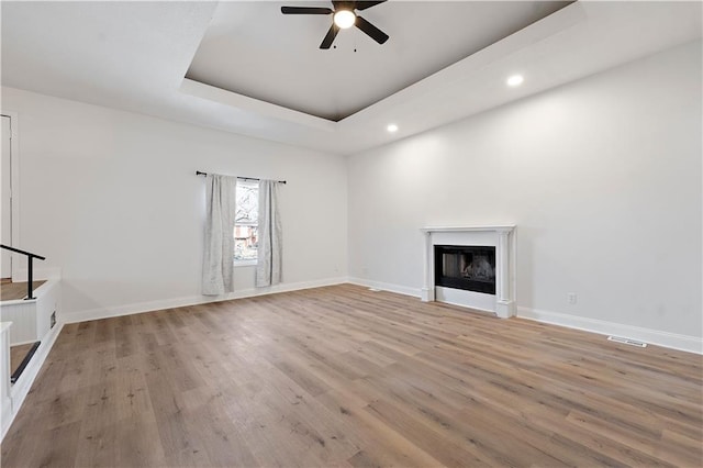 unfurnished living room featuring a tray ceiling, ceiling fan, and light wood-type flooring