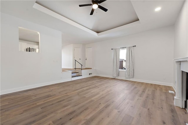 unfurnished living room with ceiling fan, a raised ceiling, and light hardwood / wood-style floors