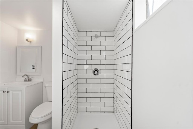 bathroom featuring a tile shower, vanity, and toilet