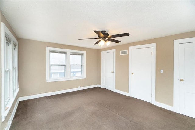 unfurnished bedroom with ceiling fan, two closets, and dark carpet