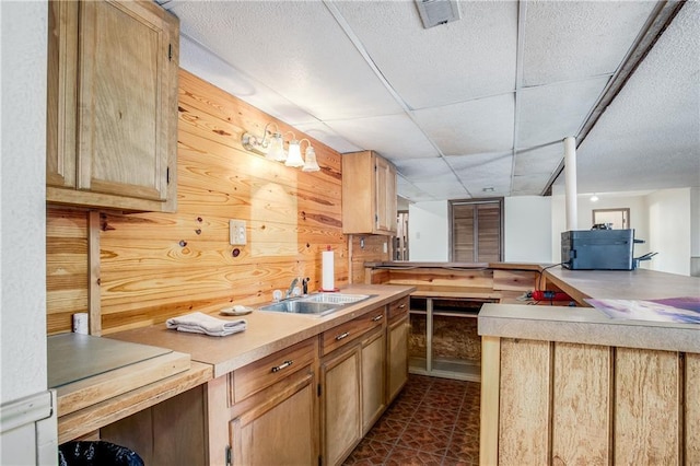 kitchen featuring light brown cabinetry, sink, a paneled ceiling, wooden walls, and kitchen peninsula