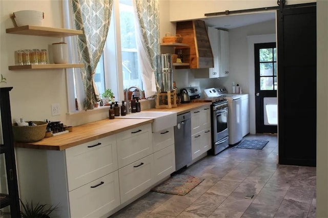 kitchen with sink, wooden counters, appliances with stainless steel finishes, washer and clothes dryer, and white cabinets