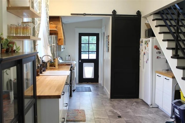 kitchen featuring white cabinetry, wooden counters, stainless steel range, a barn door, and white refrigerator with ice dispenser