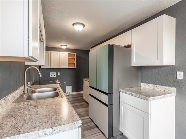 kitchen with sink, stainless steel fridge, white cabinetry, hardwood / wood-style floors, and a textured ceiling