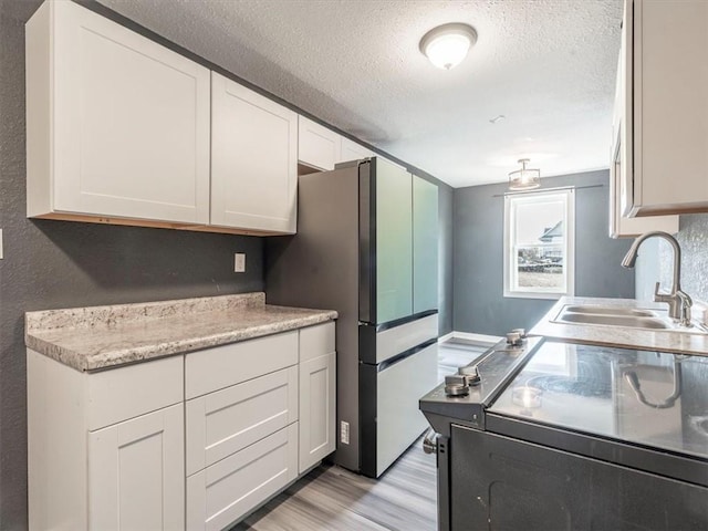 kitchen featuring sink, white cabinetry, a textured ceiling, stainless steel fridge, and light hardwood / wood-style floors