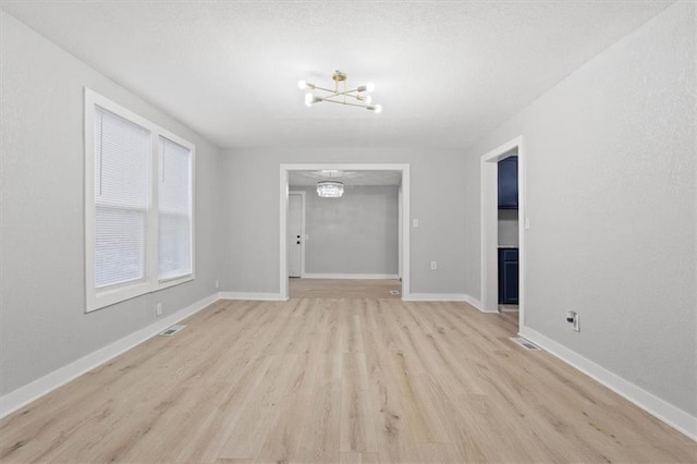 empty room featuring a notable chandelier and light wood-type flooring