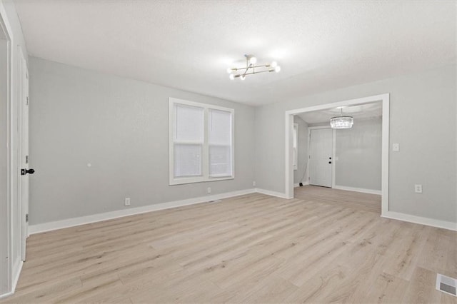 unfurnished room with an inviting chandelier, light hardwood / wood-style floors, and a textured ceiling