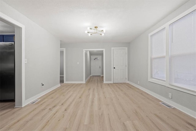 unfurnished room with a notable chandelier and light wood-type flooring