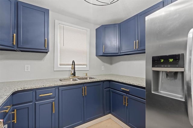 kitchen with blue cabinets, sink, light stone countertops, and stainless steel refrigerator with ice dispenser