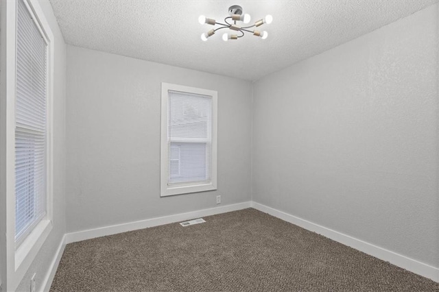 carpeted empty room featuring a notable chandelier and a textured ceiling