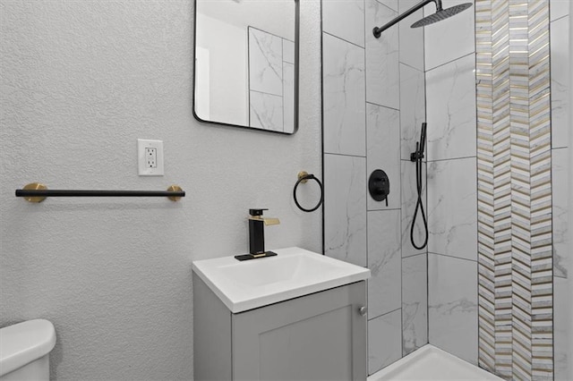 bathroom with vanity, toilet, and tiled shower