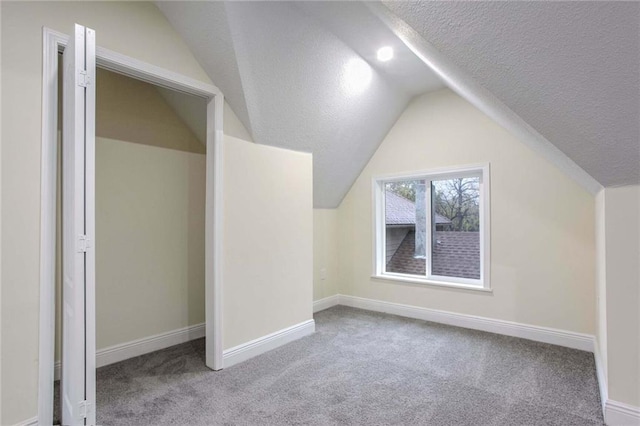 additional living space featuring vaulted ceiling, light colored carpet, and a textured ceiling