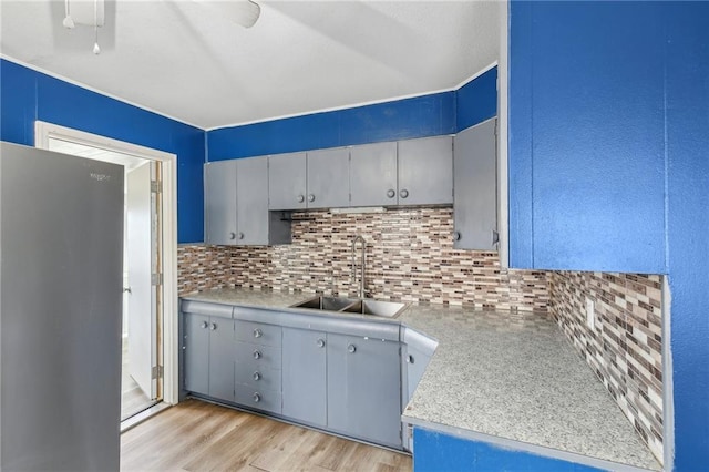 kitchen with blue cabinets, sink, stainless steel fridge, backsplash, and light wood-type flooring