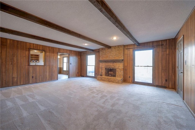 unfurnished living room with beam ceiling, wood walls, light carpet, a textured ceiling, and a fireplace