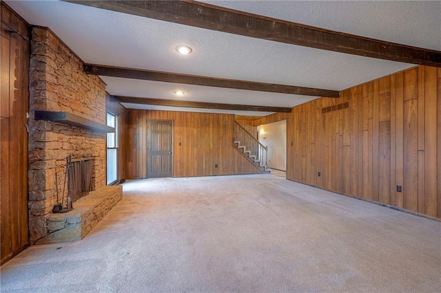 unfurnished living room with a stone fireplace, wooden walls, beamed ceiling, light carpet, and a textured ceiling