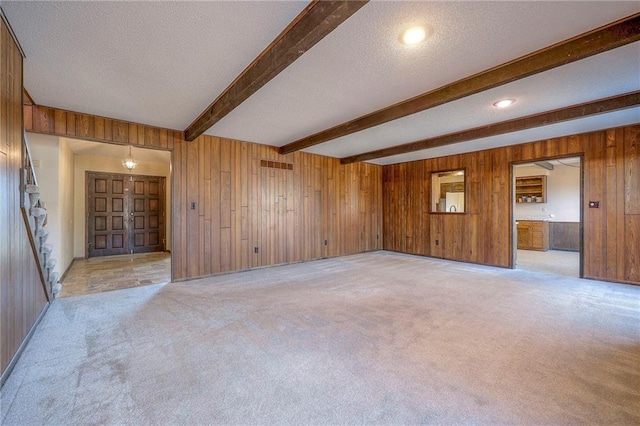 empty room featuring light colored carpet, beam ceiling, and wood walls