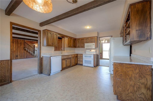 kitchen with wooden walls, white appliances, beam ceiling, and sink