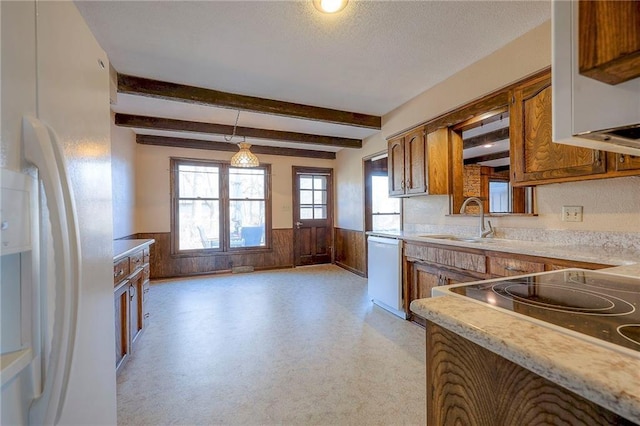 kitchen with sink, white appliances, hanging light fixtures, beam ceiling, and wooden walls