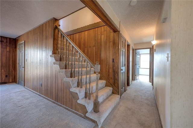 stairway featuring carpet floors, a textured ceiling, and wood walls