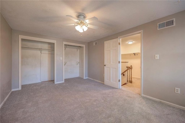 unfurnished bedroom featuring multiple closets, light colored carpet, a textured ceiling, and ceiling fan