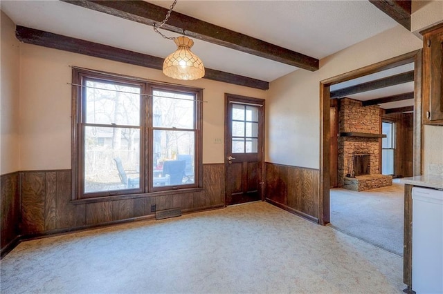 empty room featuring beamed ceiling, light colored carpet, wooden walls, and a stone fireplace