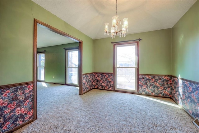 carpeted empty room featuring lofted ceiling and a notable chandelier