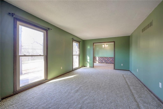 carpeted spare room with an inviting chandelier and a textured ceiling