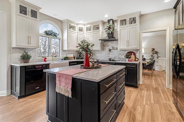 kitchen with black appliances, white cabinetry, a kitchen island, and wall chimney exhaust hood