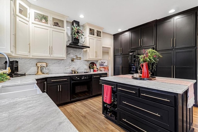 kitchen with white cabinets, decorative backsplash, light hardwood / wood-style floors, black appliances, and wall chimney exhaust hood