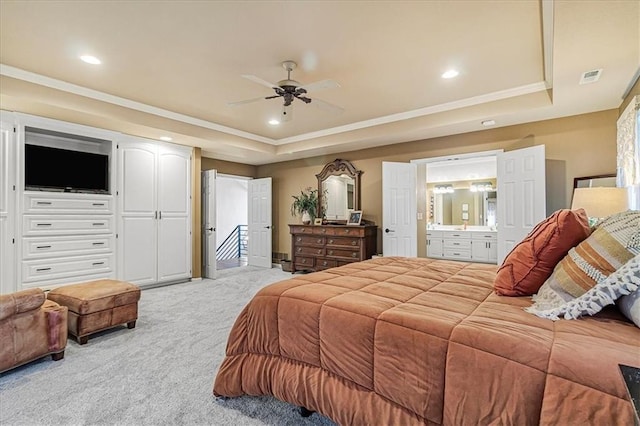 carpeted bedroom featuring crown molding, ensuite bath, a tray ceiling, and ceiling fan