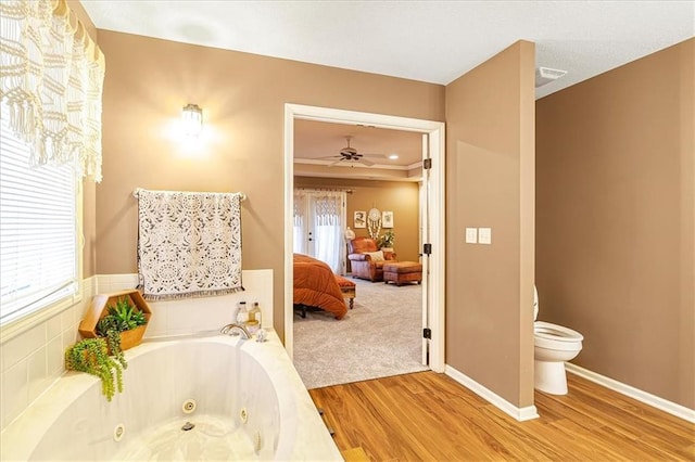 bathroom with hardwood / wood-style floors, a bathtub, ceiling fan, a tray ceiling, and toilet