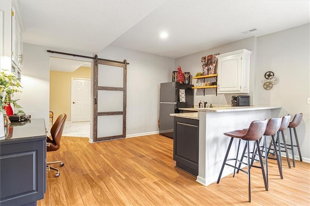 kitchen with light hardwood / wood-style flooring, white cabinetry, black refrigerator, a kitchen bar, and a barn door