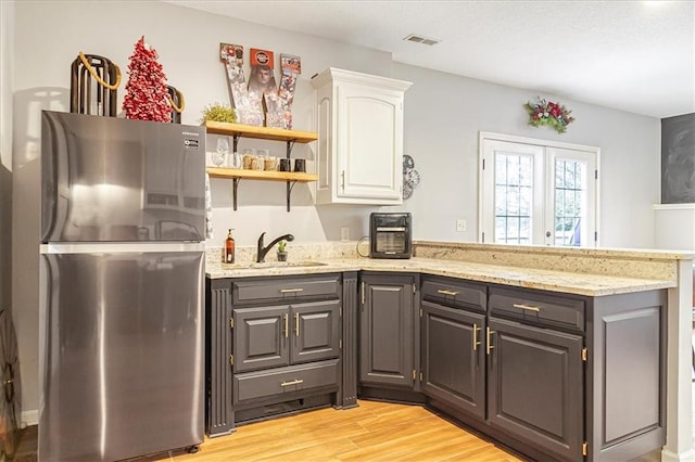 kitchen with sink, stainless steel refrigerator, light stone counters, light hardwood / wood-style floors, and white cabinets