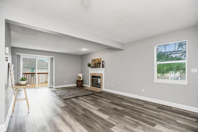 unfurnished living room featuring plenty of natural light, dark hardwood / wood-style flooring, a tiled fireplace, and a textured ceiling