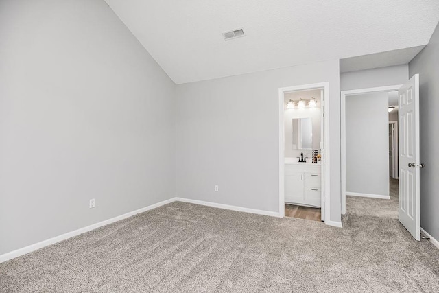 unfurnished bedroom featuring ensuite bath, lofted ceiling, carpet flooring, and sink